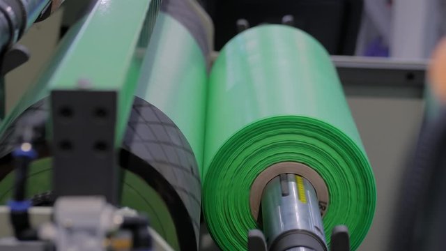 Part of automatic plastic bag making machine - moving roller with flat polyethylene green film at exhibition, trade show. Manufacturing, recycling, industry and automated technology equipment concept