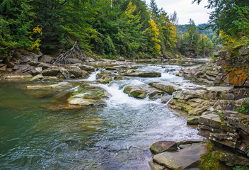 Beautiful mountain river with a fast flow. Large stones with rocks in the middle of a green forest.