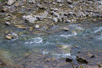 Beautiful mountain river with a fast flow. Large stones with rocks in the middle of a green forest.