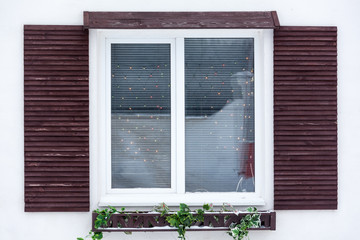 White plastic pvc window with decorative wooden shutters and Christmas lights inside, outdoor facade