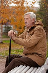 Old  man in the autumn park sitting on a bench with his walking stick.