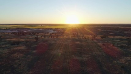 Aerial descend over Australian desert facing the setting sun with lens flare