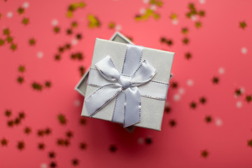 White textured gift boxes with ribbon bows surrounded by stars and snowflakes on a coral background, from above