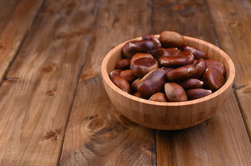 Cup of chestnuts on a wooden background. Autumn harvest and ripe fruits. Free space for text.