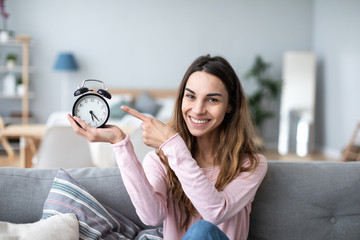 Young happy woman with clock on the couch.