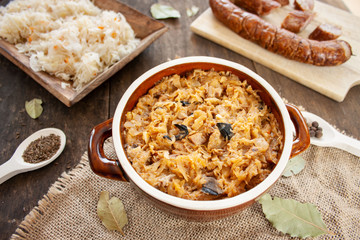 Bigos in stoneware dish, next to bigos ingredients: sausage, sauerkraut and cumin