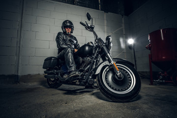 Naklejka premium Serious man in helmet and black leather suit is sitting on his motorbike.