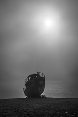 Black and white picture of a fishing boat staing on the coast during foggy morning 