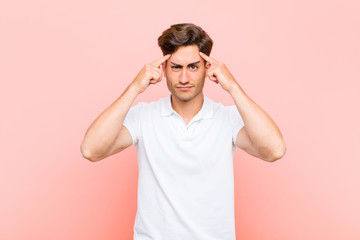 young handsome man with a serious and concentrated look, brainstorming and thinking about a challenging problem against pink background
