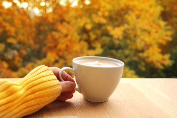 cup of cocoa with milk or cappuccino in hand on a background of yellow and orange tree leaves, autumn mood concept, close-up