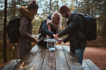 Small group of friends are assembling drone in the forestal park using wooden table.