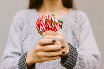 Christmas candy in the hands of a girl in a gray sweater. Lots of Christmas candy canes. Christmas striped candy canes. Green, red and white stripes. Selective focus.