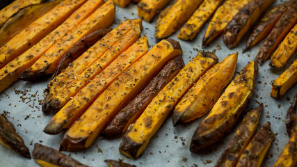 Frytki z batatów leżące na papierze do pieczenia. Zbliżenie.