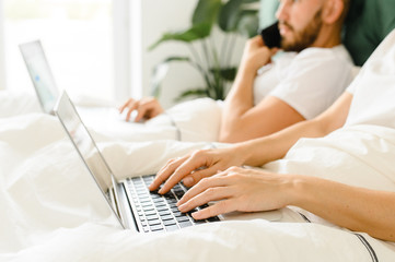 young couple uses laptop in bed. freelancer morning.