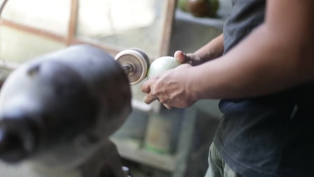 Slow motion shot of man sculpting, polishing semiprecious green sphere. Close up of hands polishing rock with disc. Handcraft decoration. La Toma, San Luis, Argentina
