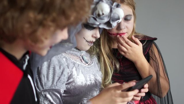 Children in suits of Dracula and the dead bride are watching photos on a smartphone. Halloween selfies, Halloween celebrations, kids and gadgets