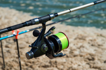 Fishing carp reel close-up on the background of water and fishing rods on stands in a bright Sunny day. Background