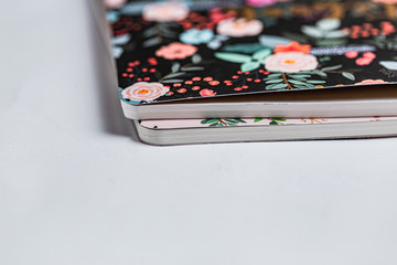 Patterned notebooks on white backdrop. Flower pattern on paper notebooks. Pink and black fancy girly things. Teenage girly pinky diary. Pink phone on white surface. Flower botanical pattern. 