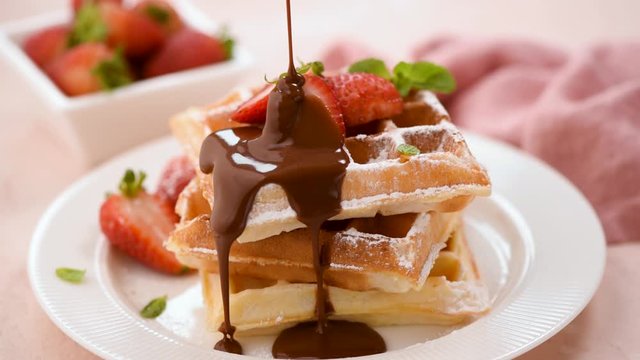 Pouring chocolate sauce on belgian waffles served with strawberries. Tasty sweet food, dessert or breakfast