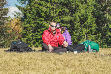 Naklejka na ściany i meble Girl and man hikers in mountains. They drink tea and coffee on top. Embrace. Campaign. Ukrainian Carpathian Mountains. Traveling in Ukraine.