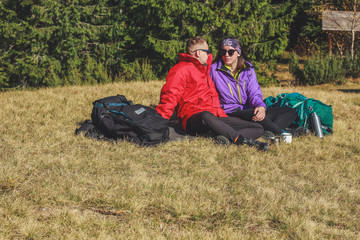 Naklejka na ściany i meble Girl and man hikers in mountains. They drink tea and coffee on top. Embrace. Campaign. Ukrainian Carpathian Mountains. Traveling in Ukraine.