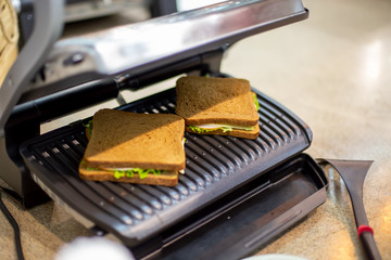 two delicious square grilled sandwiches lies in the open electric grill close-up, soft focus,...