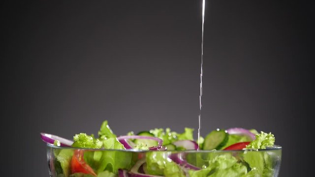 Salad in the glass bowl. Stream of golden oil is pouring down. Nobody in the frame. A lot of copyspace.