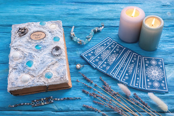 Blue tarot cards deck and white magic book on blue wooden table background.