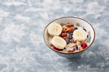 Bowl of granola with milk, nuts, raisins and banana. Concept for a tasty and healthy meal. Rustic wooden background. Copy space. 