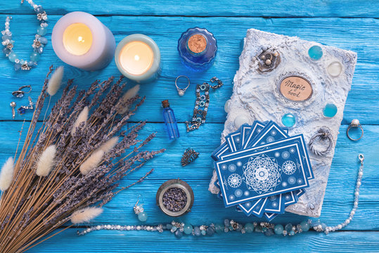 Blue tarot cards deck and white magic book on blue wooden table background.