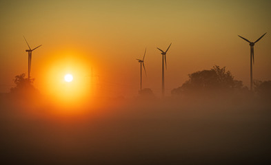 Obraz premium Wind turbines in the background of dawn in the fog.