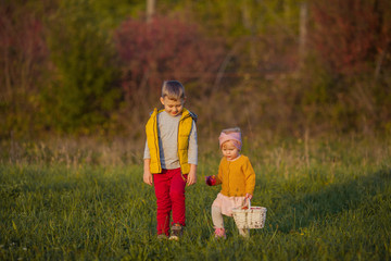 Little cute boy and girl are playing in the autumn garden. Brother and sister with red apples. Warm and bright autumn.