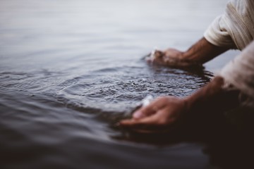 Closeup shot of a person wearing a biblical robe washing his hands in the water