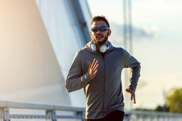 Attractive fit man running fast along big modern bridge. Exercising, Jogging, Sport, Winter. Male athlete running.