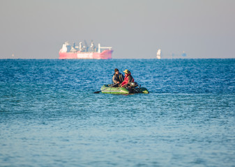 Ukraine, Odessa - August 12, 2019: Fishermen in a rubber boat at sea with a cargo ship.