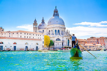 Gondolier and gondola on Grand Canal, Basilica Santa Maria della Salute in Venice, Italy. Sunny summer day with blue sky. 