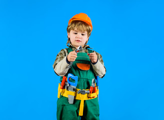 Little kid boy in builder uniform with wrench. Child game. Kid repairman with tool belt holds wrench. Builder boy in helmet and tools for building. Work with tools. Repair. Boy as builder or repairer.