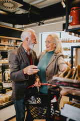 Happy senior couple shopping in grocery store or supermarket. Consumerism concept.