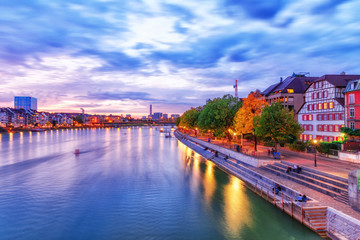 Besel, Switzerland, autumn. Beatiful twilight cityscape of Swiss city Basel, view over  Rhine river beneath incredible dramatic sky. City lights of Basel, popular travel and business destination.