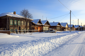 Snow-covered village street in winter. Traditional wooden houses. Village of Visim, Sverdlovsk region, Russia.