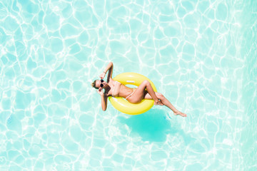 Top view of slim young woman in bikini on the yellow air inflatable ring in the big swimming pool.