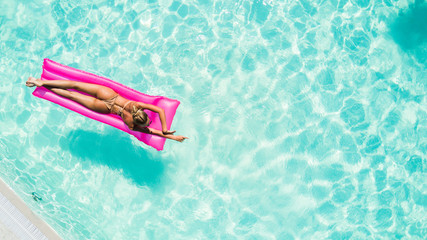 Enjoying suntan. Vacation concept. Top view of slim young woman in bikini on the pink air mattress in the big swimming pool.