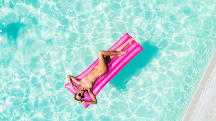 Sexy young woman takes a sunbath on a pink float in the pool,. Aerial shot