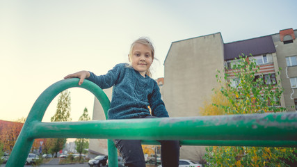 A charming little girl in casual clothes sits on a metal structure in the yard.