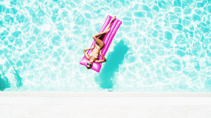 Sexy woman rest and sunbath on a float in the pool, top view aerial shot. Young woman in a bikini swimsuit floating on an inflatable pink mattress top view