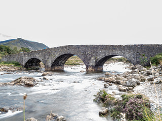 Fototapeta na wymiar Old stone bridge across the river in cloudy weather, Isle of Skye, Scotland