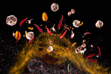 Hot red pepper, garlic, different spices powder flying on a black background Motion freeze photo...