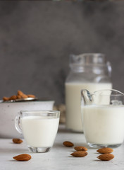 Organic almond milk in glass jugs with ingredients on a light grey background. Healthy and vegan eating. Alternative type of milk.