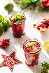 Fresh cold purple lemonade or cocktail with mint, pomegranate, lime and ice in glass in in the morning light, sunlight shadow. Christmas or New Year concept. Trendy style with artistic shadows.