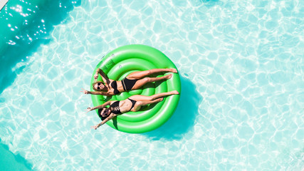 Aerial view of two women lying on inflatable green mattress floating and relaxing in pool